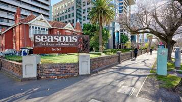 A Seasons Heritage Melbourne hotel sign with a brick wall and a pathway leading to the entrance.