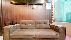 A brown sofa in a room with wooden paneling and a window with a green curtain. - Komfort Inn (Pune)