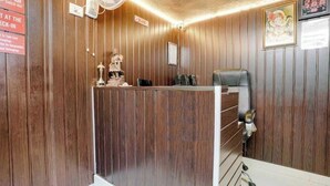 A reception area with a wooden panel wall, a reception desk, a statue, and a sign indicating check-in and check-out times. - Komfort Inn (Pune)