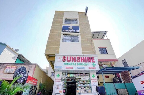 Een gebouw met een bord voor 'ROYAL KOMFORT INN' en een apotheek genaamd 'SUNSHINE CHEMIST & DRUGGIST' met afdelingen voor reguliere geneeskunde, ayurveda, chirurgie en cosmetica.