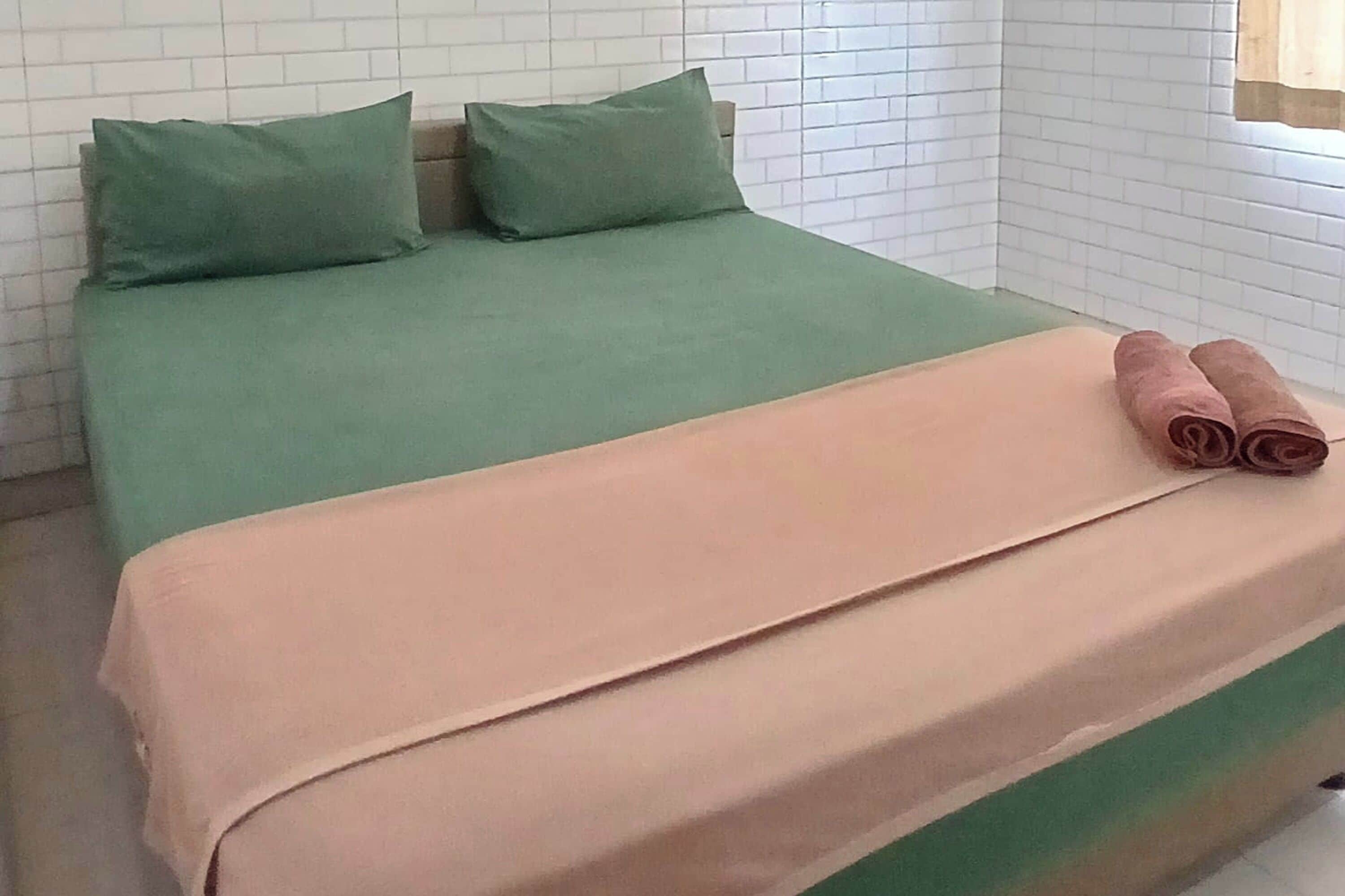 Een bed met groen en beige beddengoed, twee kussens en twee opgerolde handdoeken.