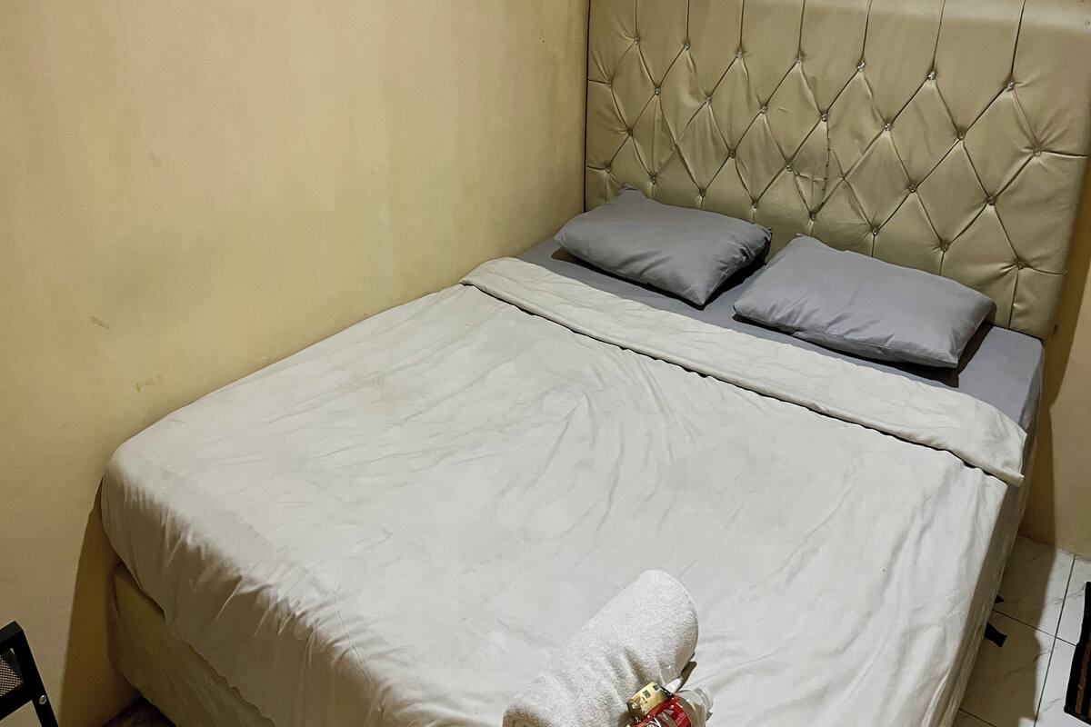 Una cama bien hecha con un cabecero capitonado, dos almohadas y una manta blanca.