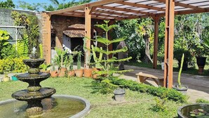 A garden with a stone fountain, potted plants, and a wooden pergola. - Annet Homestay (Sleman)