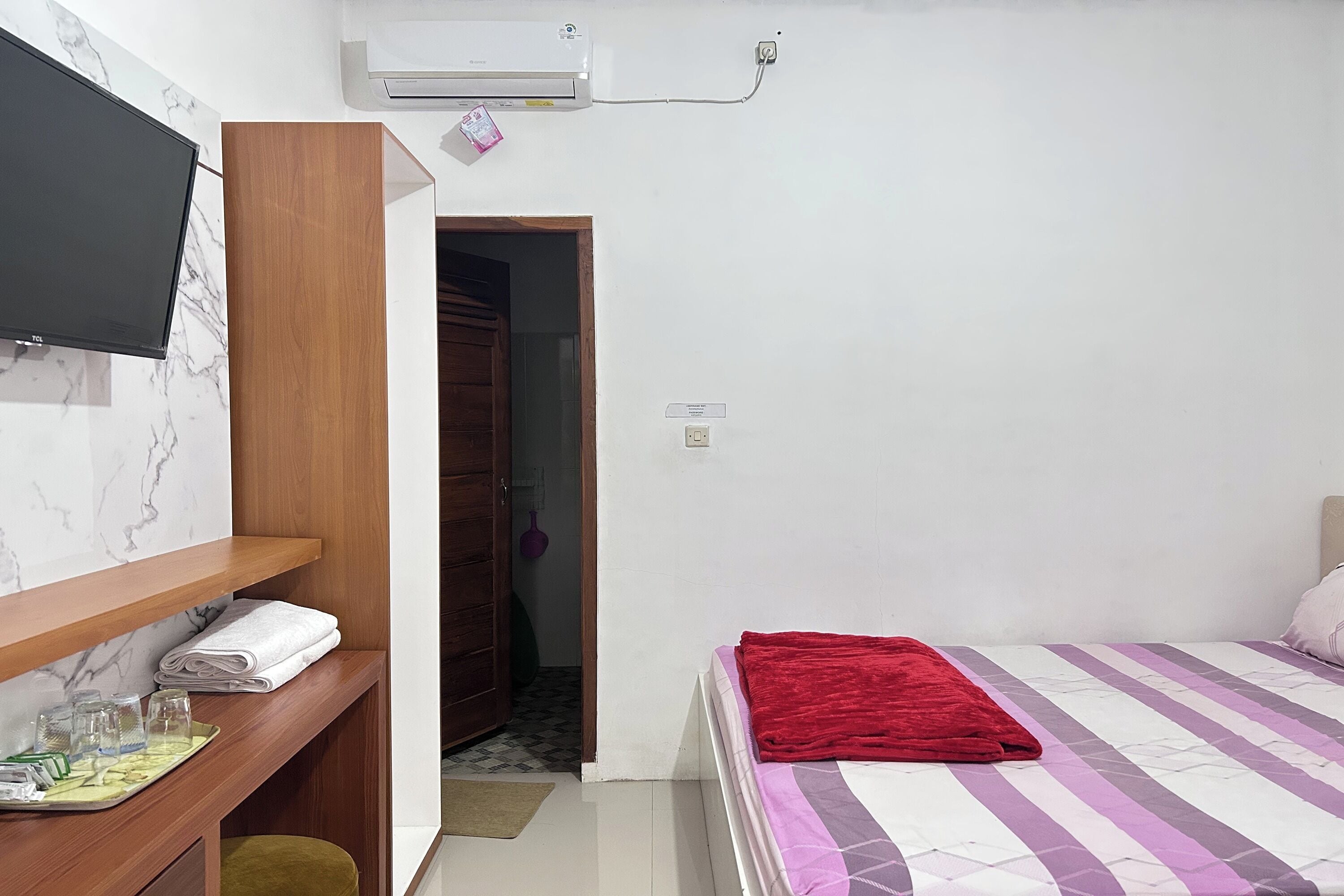 Ein Schlafzimmer mit Bett, einem an der Wand befestigten Fernseher, einem Holztisch und einem Kleiderschrank.