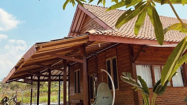A wooden house with a tiled roof, a covered patio, and potted plants. - Annet Homestay (Sleman)