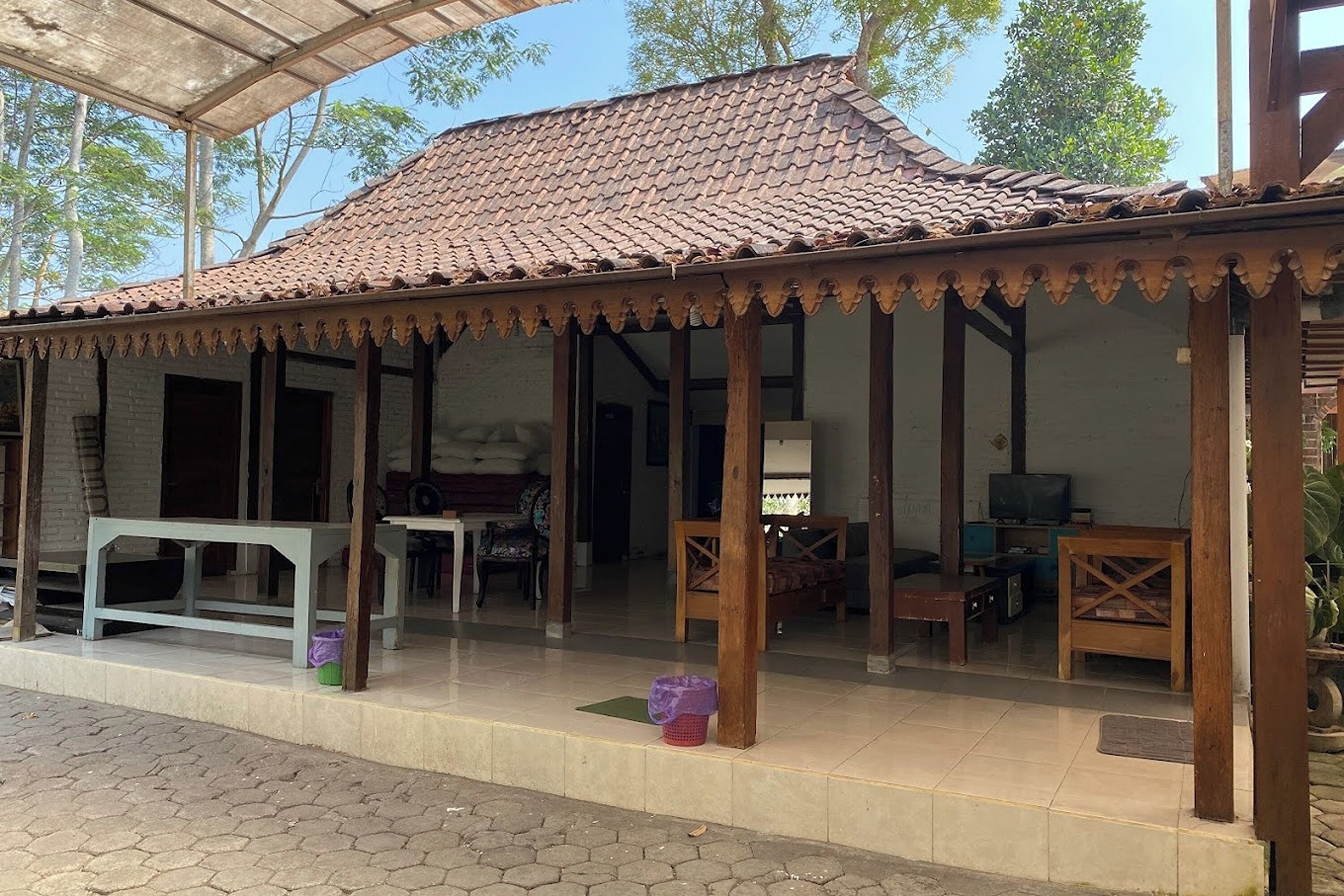 A covered outdoor area with a tiled roof, wooden pillars, and a bench.