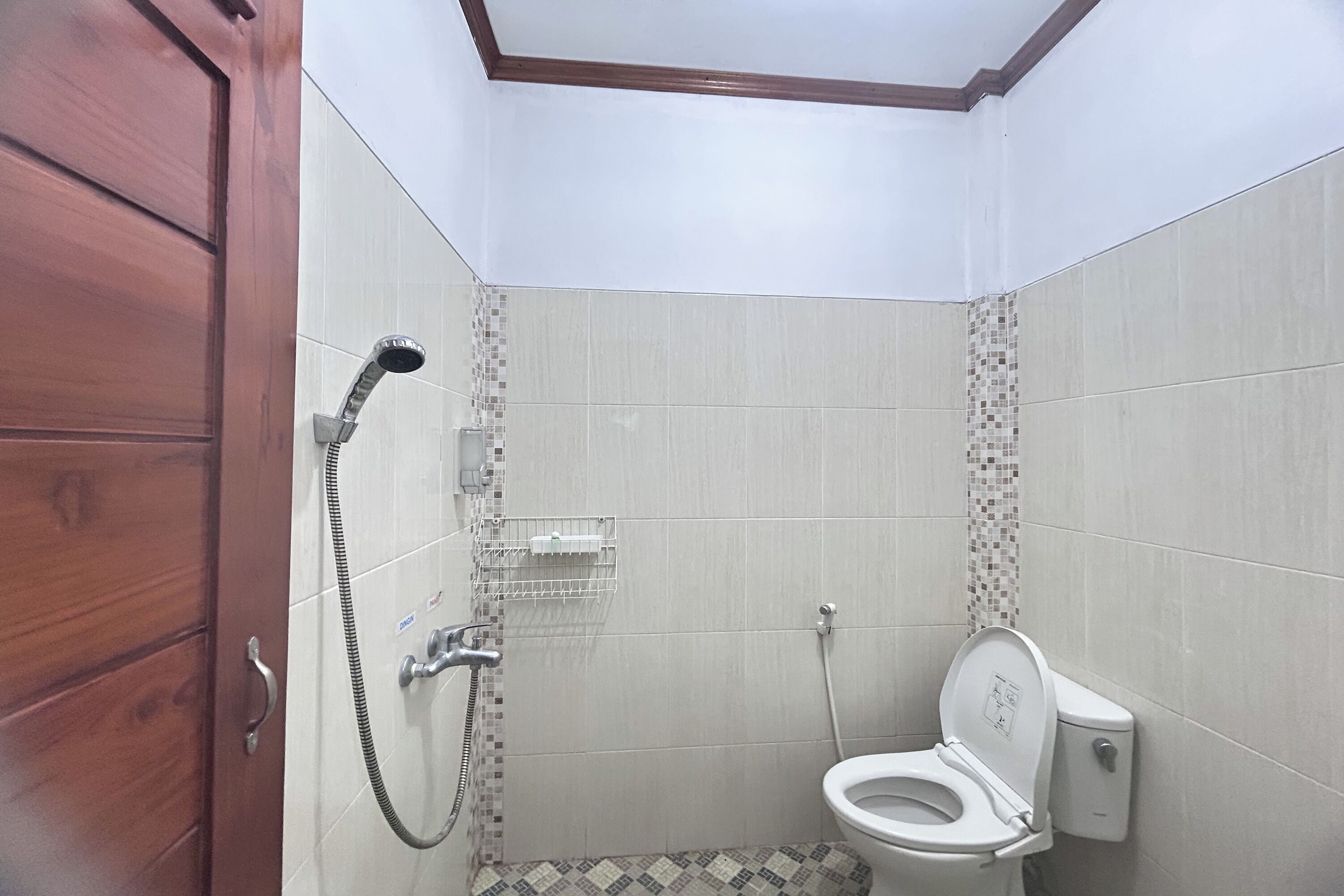 Egy kis fürdőszoba, amelyben WC, zuhanyzó és egy fa szekrény található.