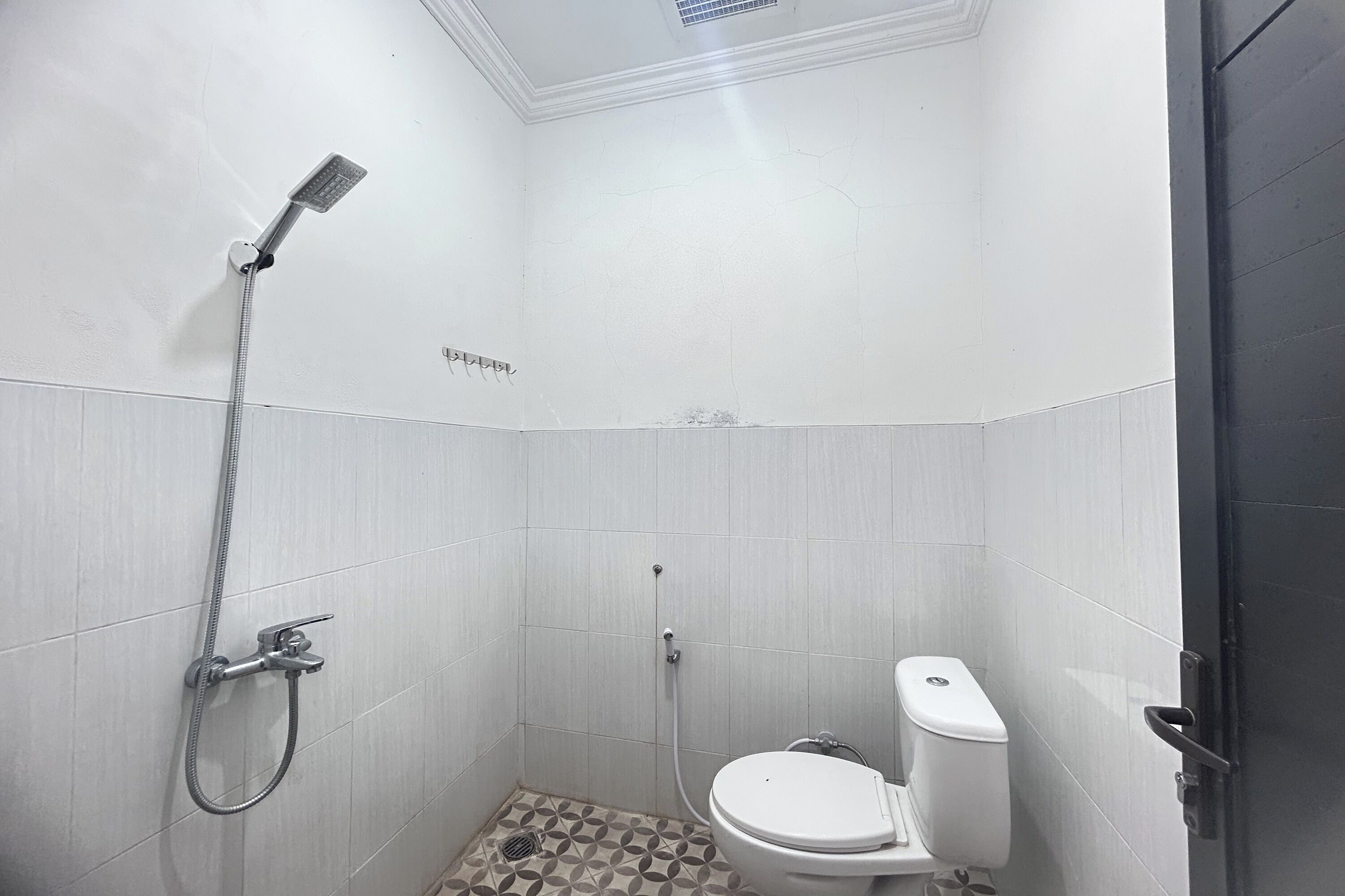 A small, white-walled bathroom with a shower, toilet, and a tiled floor.