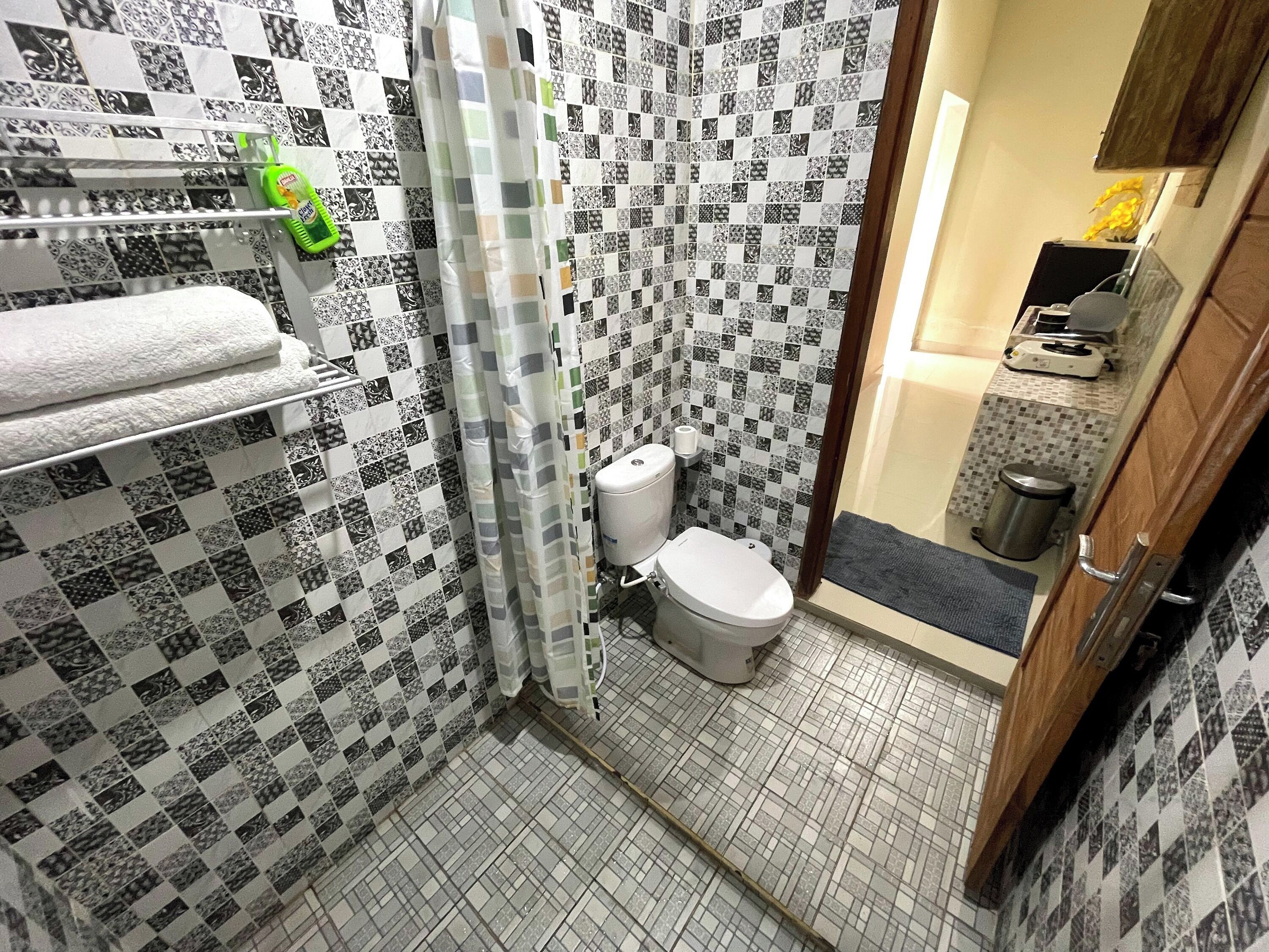 Ein Badezimmer mit Schachbrettmuster auf den Fliesen, einer Toilette, einem Duschvorhang und einem Handtuchhalter mit einer grünen Flasche.