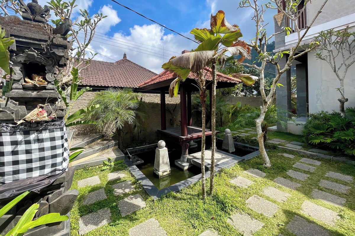Un cortile con un piccolo stagno, gradini in pietra e una struttura tradizionale balinese.