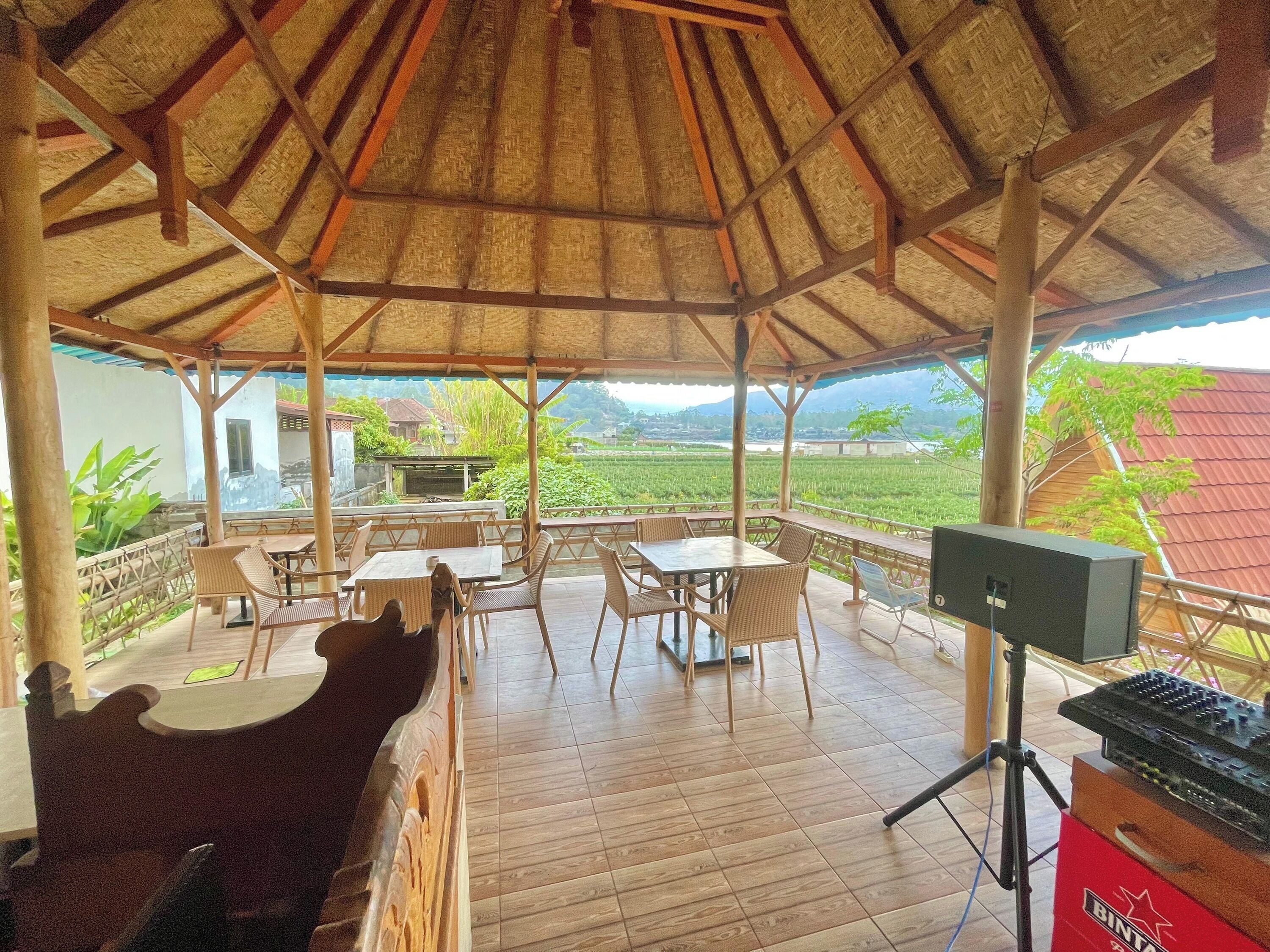 A covered outdoor seating area with tables and chairs, a DJ setup, and a view of a lush landscape.