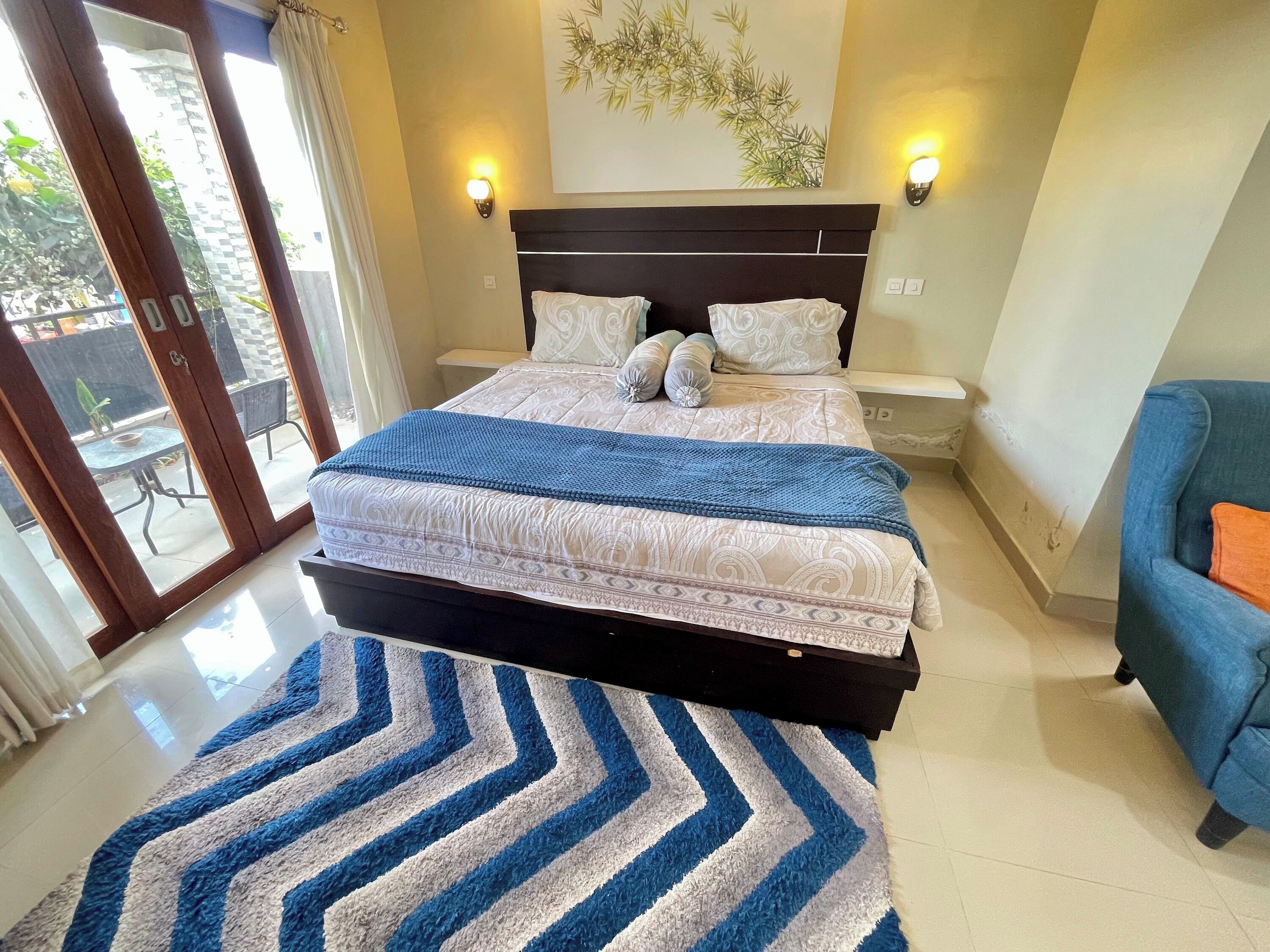 A bedroom with a bed, nightstands, a blue chair, and a view through a glass door.