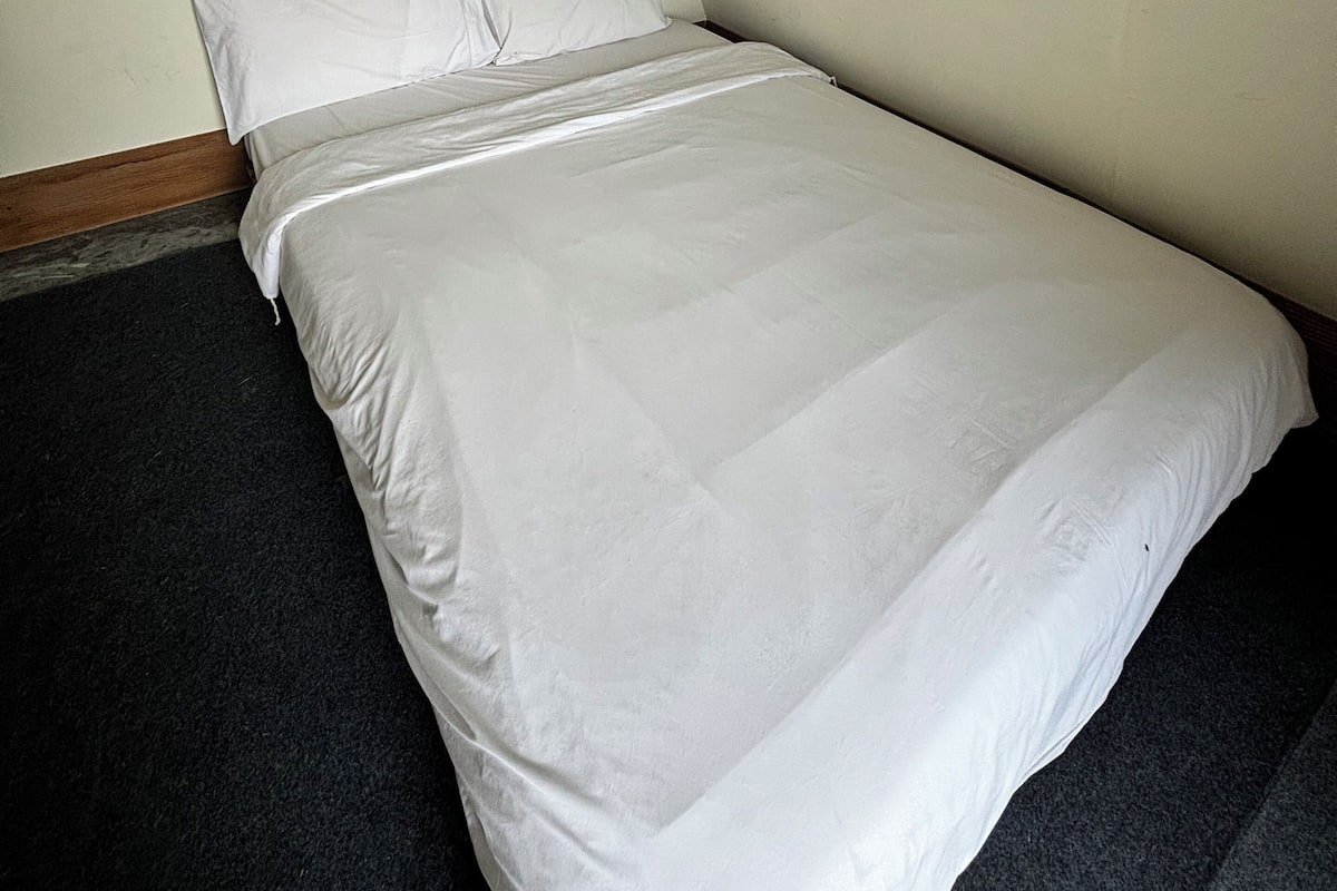 A single bed with white bedding in a room with plain walls and a dark carpet.
