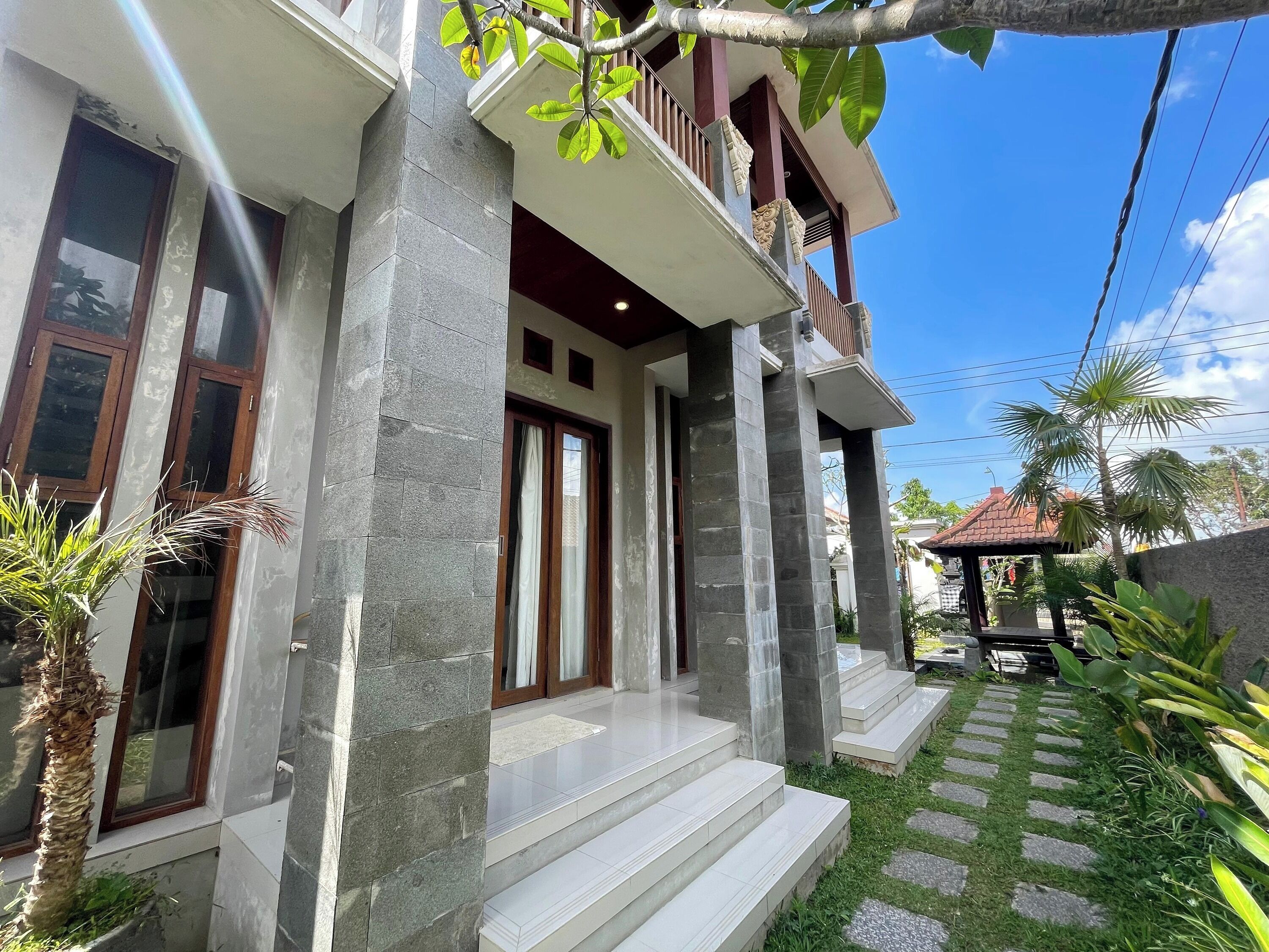A modern house with stone pillars, a balcony, and a well-maintained garden with a stone pathway.
