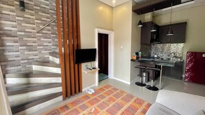 A modern apartment with a staircase, a kitchen with bar stools, a flat-screen TV, and a patterned rug. - Double U Camp And Villa (Kintamani)
