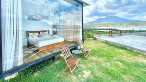 A modern bedroom with a glass wall, a bed, and a view of a lake and mountains. - Double U Camp And Villa (Kintamani)
