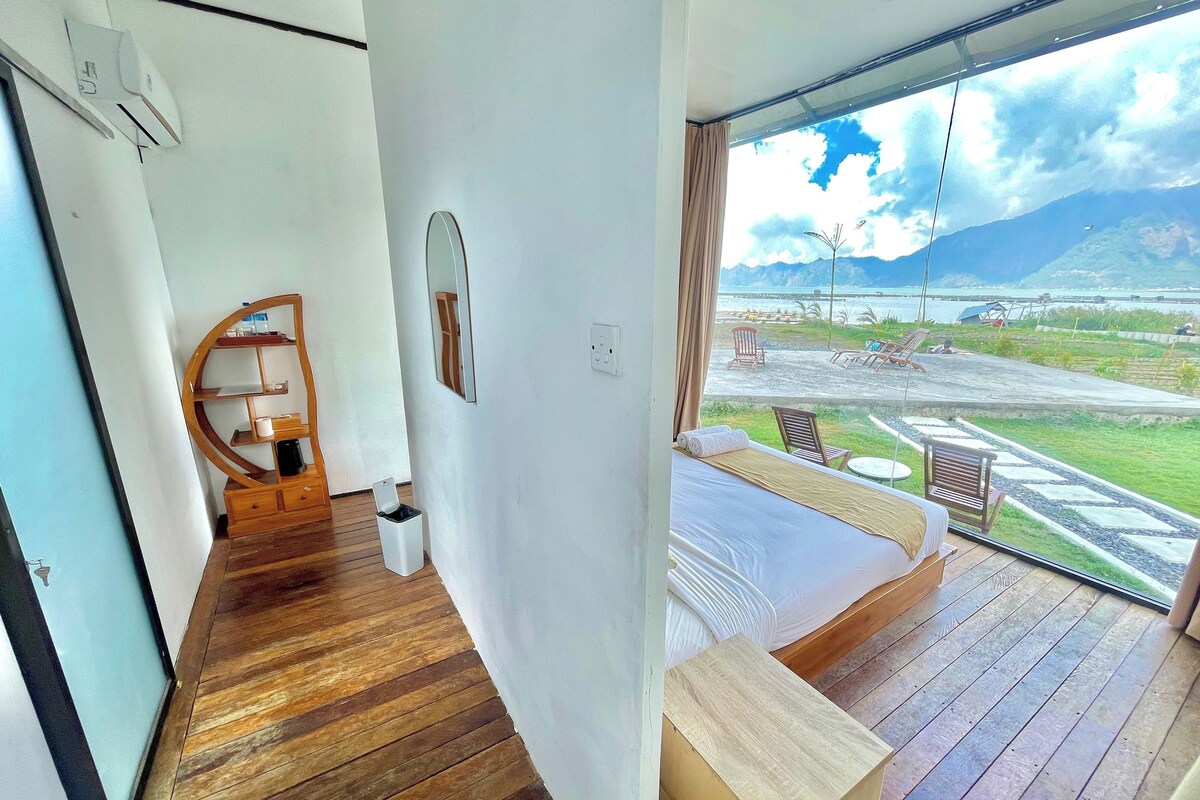 Ein Schlafzimmer mit Holzboden, einem Bett, einem kleinen Holztisch, einem Spiegel und Blick auf Strand und Berge.