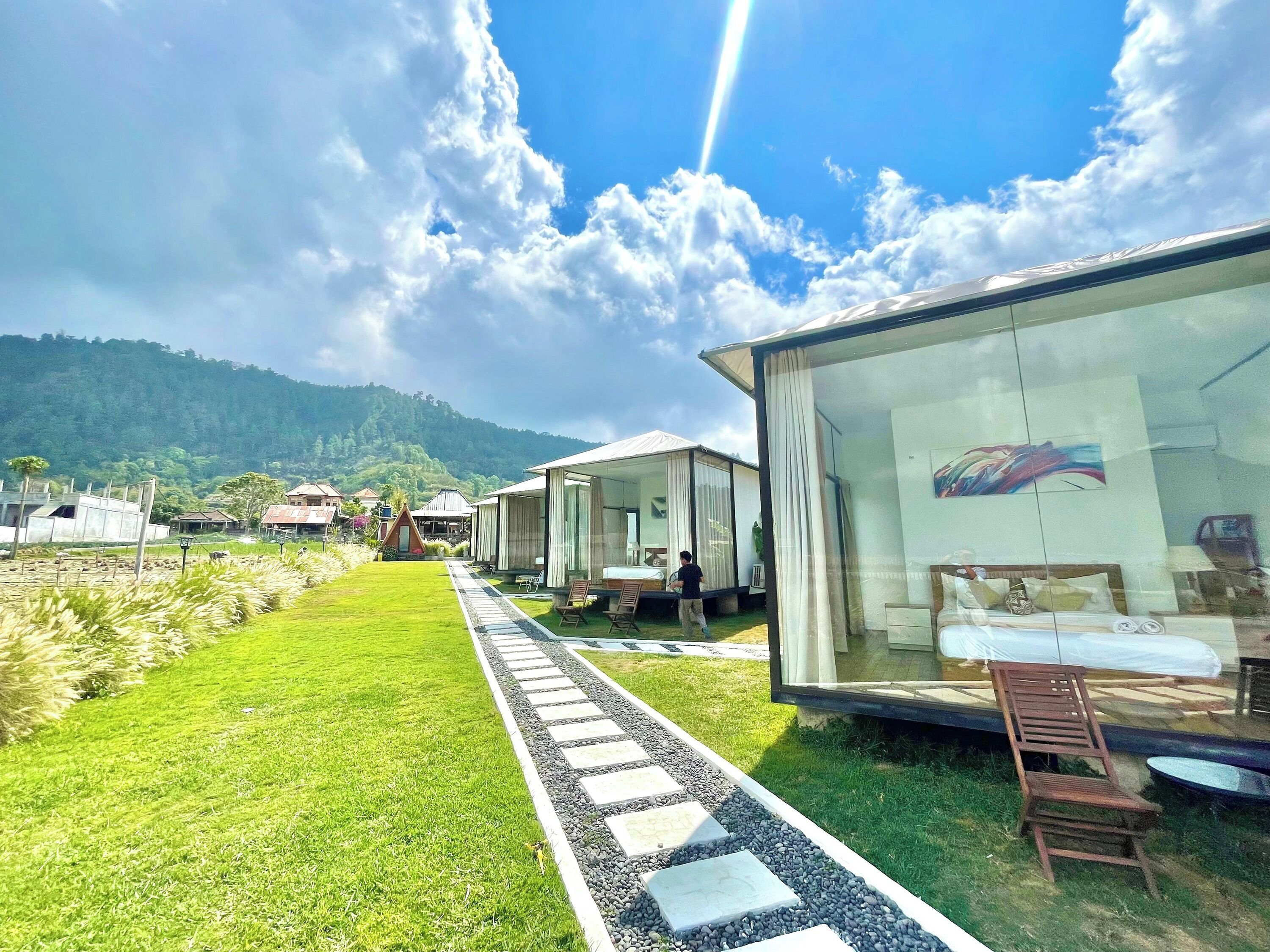 A modern resort with glass-walled rooms, a well-maintained lawn, and a clear view of the surrounding hills.