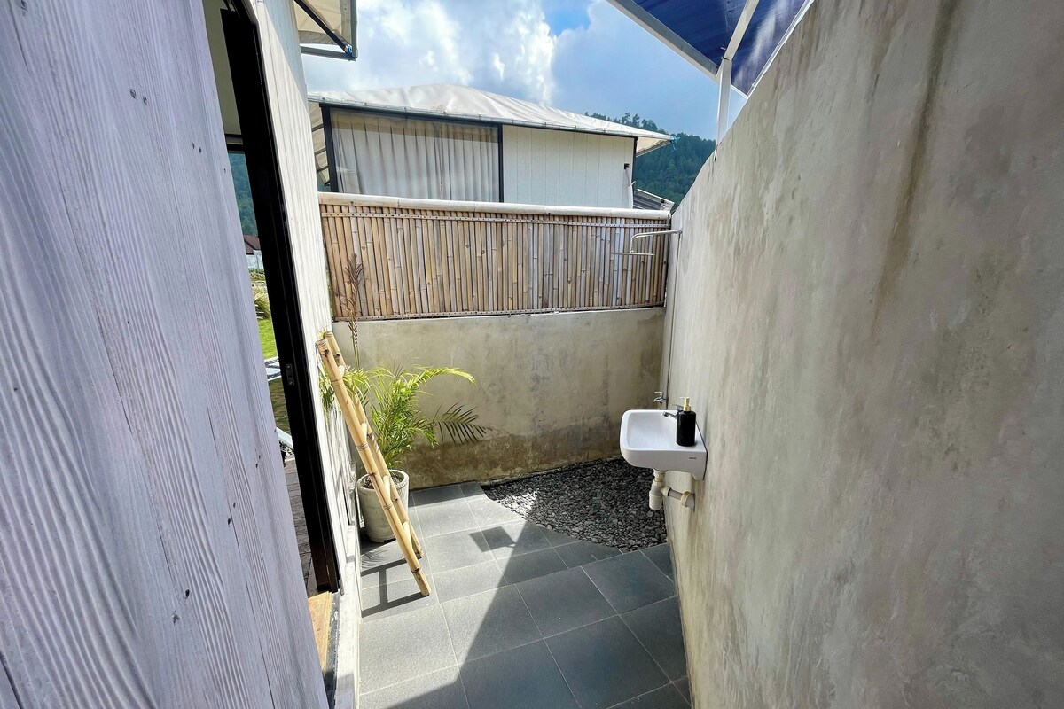 A small outdoor bathroom with a white sink, bamboo plant, and a wooden fence.