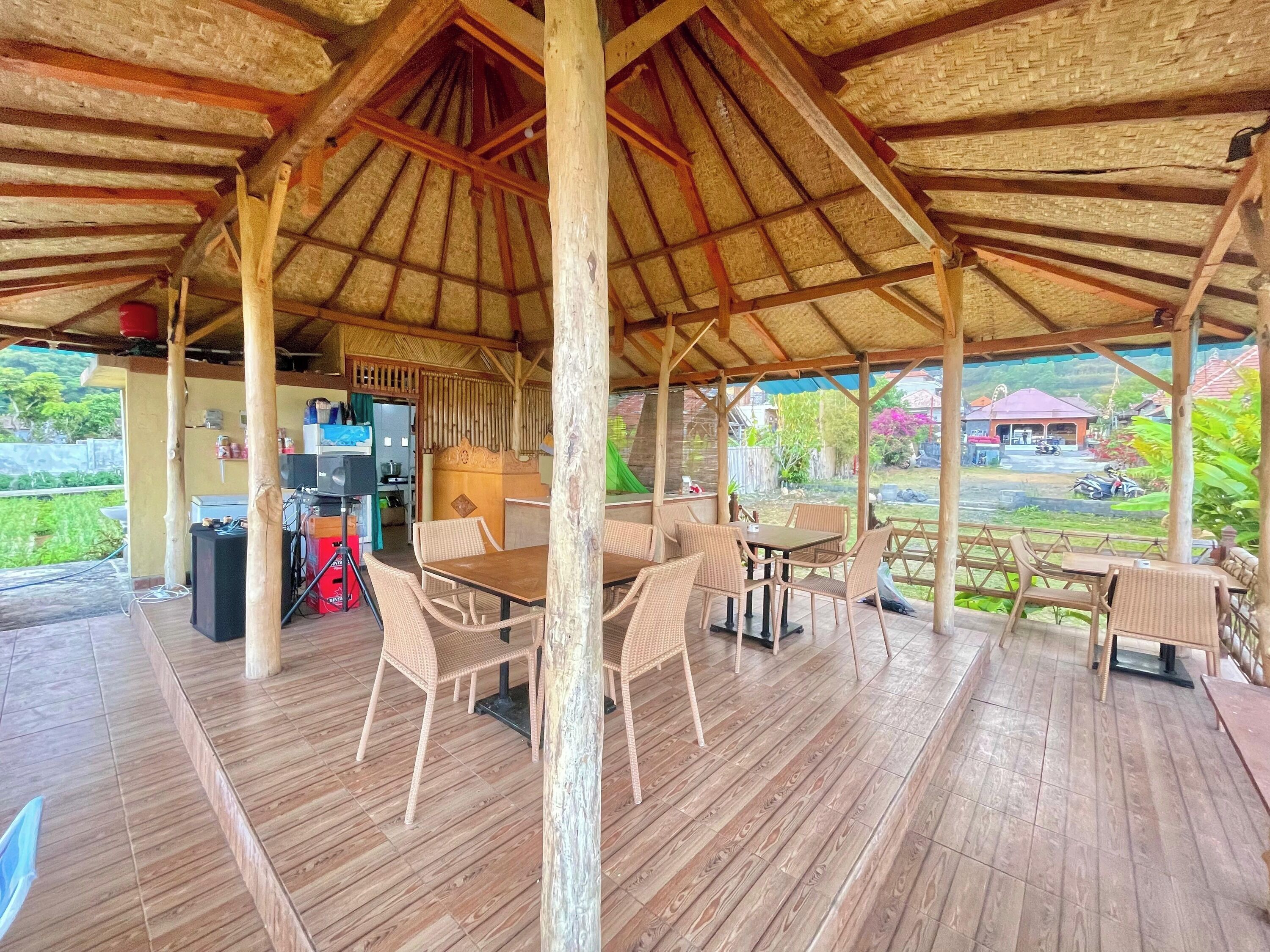 A covered outdoor area with wooden flooring, wicker furniture, and a thatched roof.