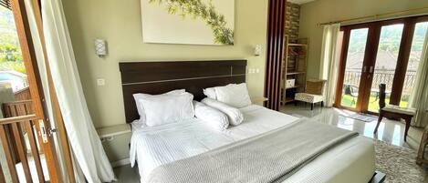 A spacious bedroom with a large bed, a wooden headboard, a view of the outdoors through a sliding door, and a wall-mounted artwork.