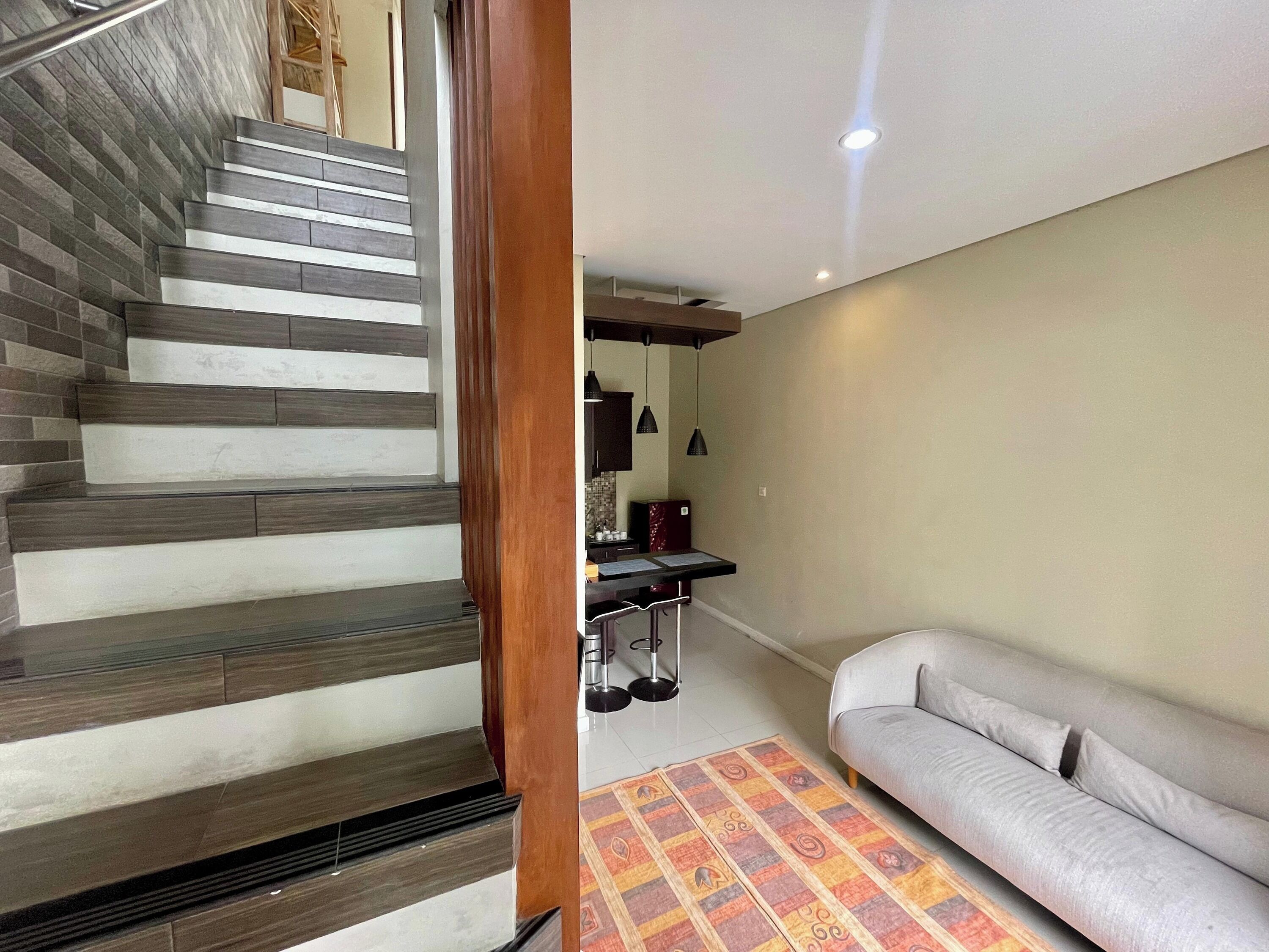 A staircase with alternating dark and light steps, a sofa, a patterned rug, and a kitchen area with cabinets and a hanging light fixture.