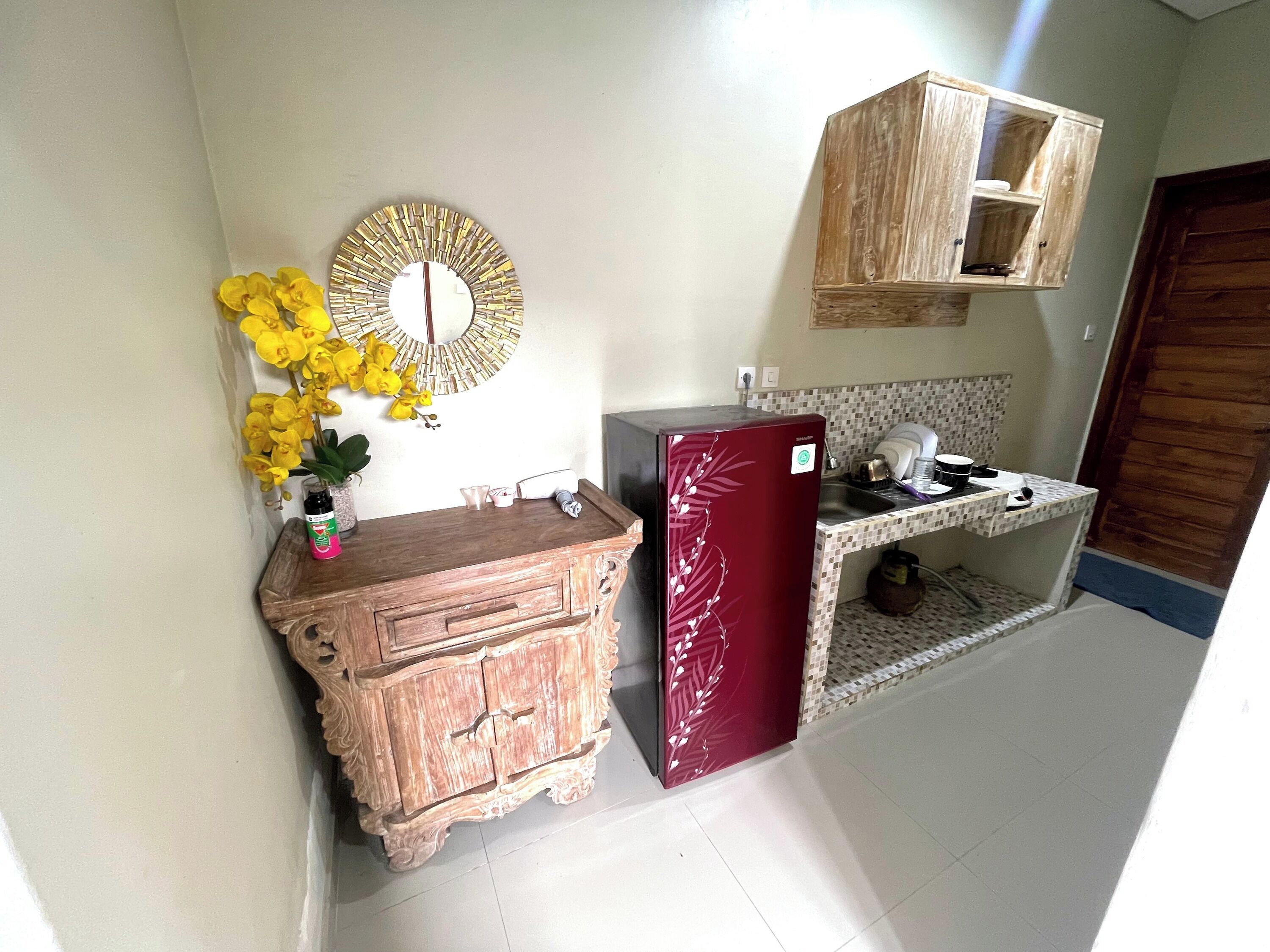 Una cocina compacta con un armario de madera, un refrigerador, un lavamanos y un espejo decorativo.