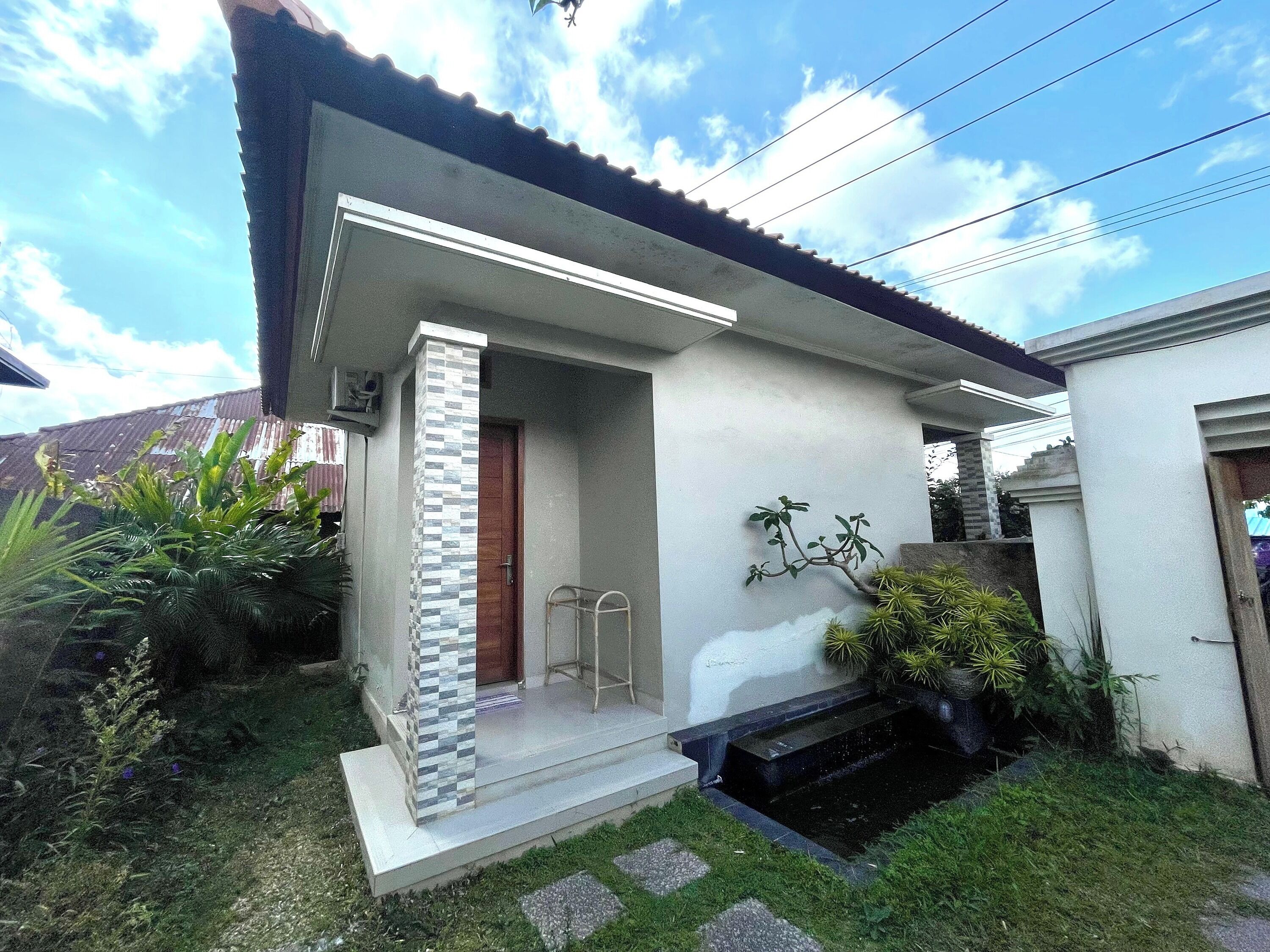 A modern house with a tiled entrance, a small porch, and a garden with various plants.