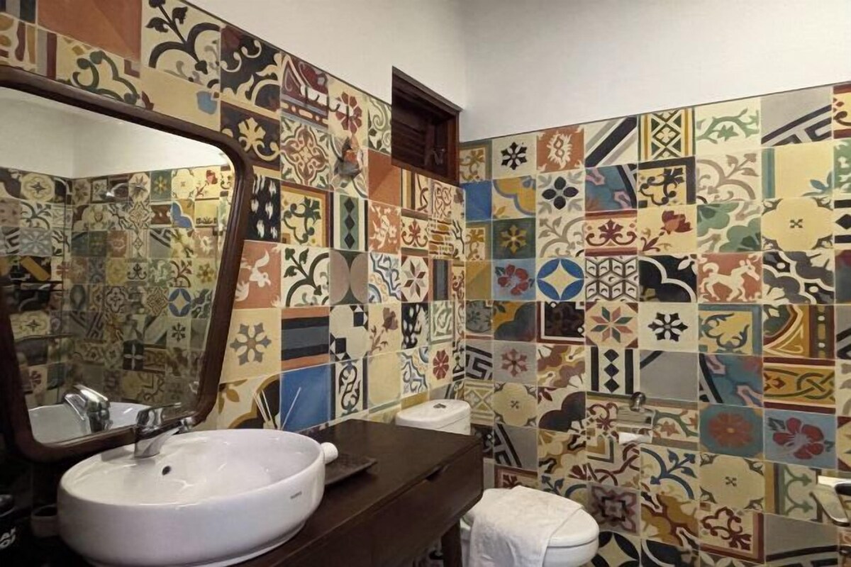 Un baño con un lavamanos blanco, un espejo y un inodoro. Las paredes están decoradas con una variedad de azulejos coloridos.