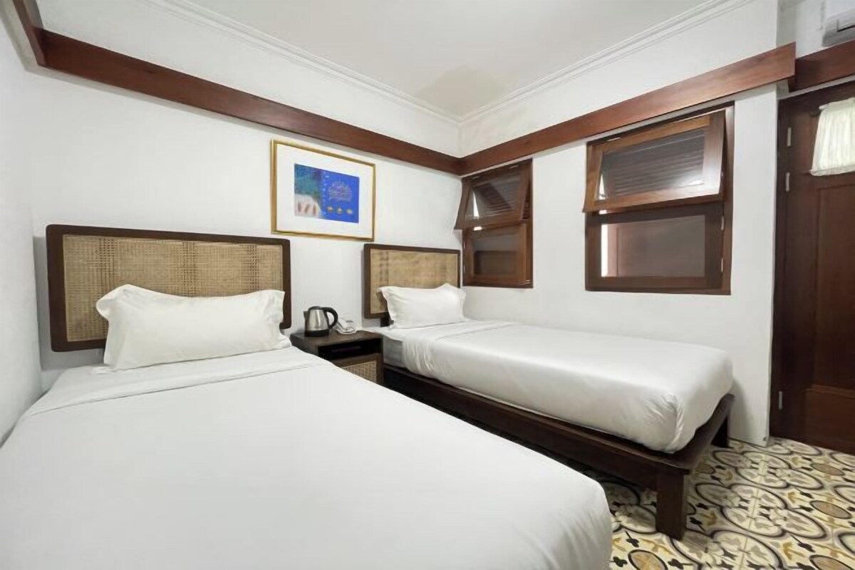 Habitación de hotel con dos camas individuales, cabecera de madera, un cuadro en la pared y piso estampado.