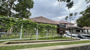 A building with a tiled roof, a sign reading "EMHM," and a fenced area with greenery.