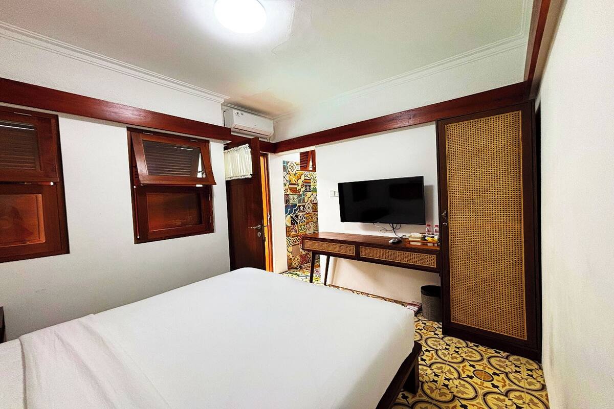 Een hotelkamer met een bed, een televisie, een bureau met een computer en een raam met zonwering.