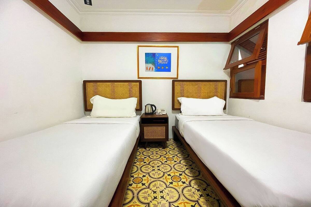 Een hotelkamer met twee eenpersoonsbedden, een tafeltje met een waterkoker en een vloer met een patroon.