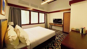 A hotel room with a bed, a desk with a television, and a patterned carpet.