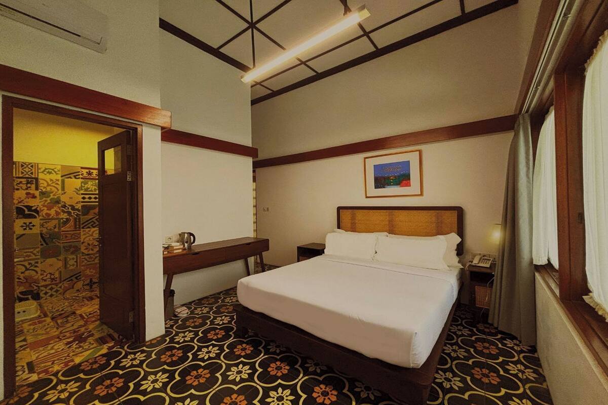 Een hotelkamer met een bed, bureau, stoel, telefoon en een foto aan de muur.