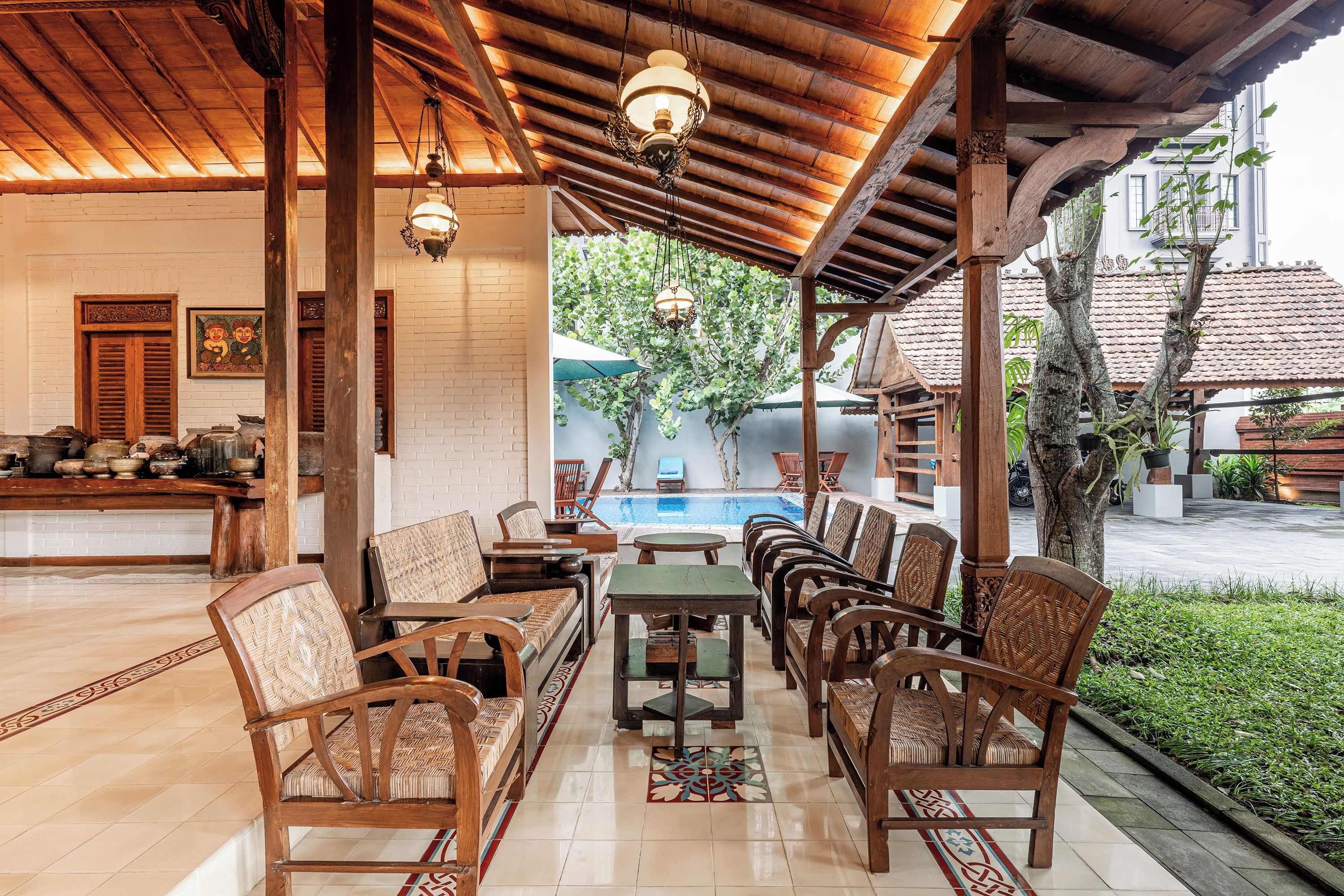 A covered outdoor seating area with wooden furniture and a pool in the background.