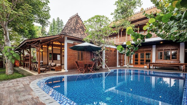 Ein Swimmingpool mit gefliestem Rand, einer Holzterrasse und einem überdachten Sitzbereich mit Stühlen und Tischen.