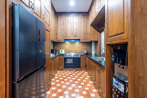 A kitchen with wooden cabinets, a black refrigerator, a stove, and a tiled floor. - Joglo Wardani By Zuzu (Ngaglik)