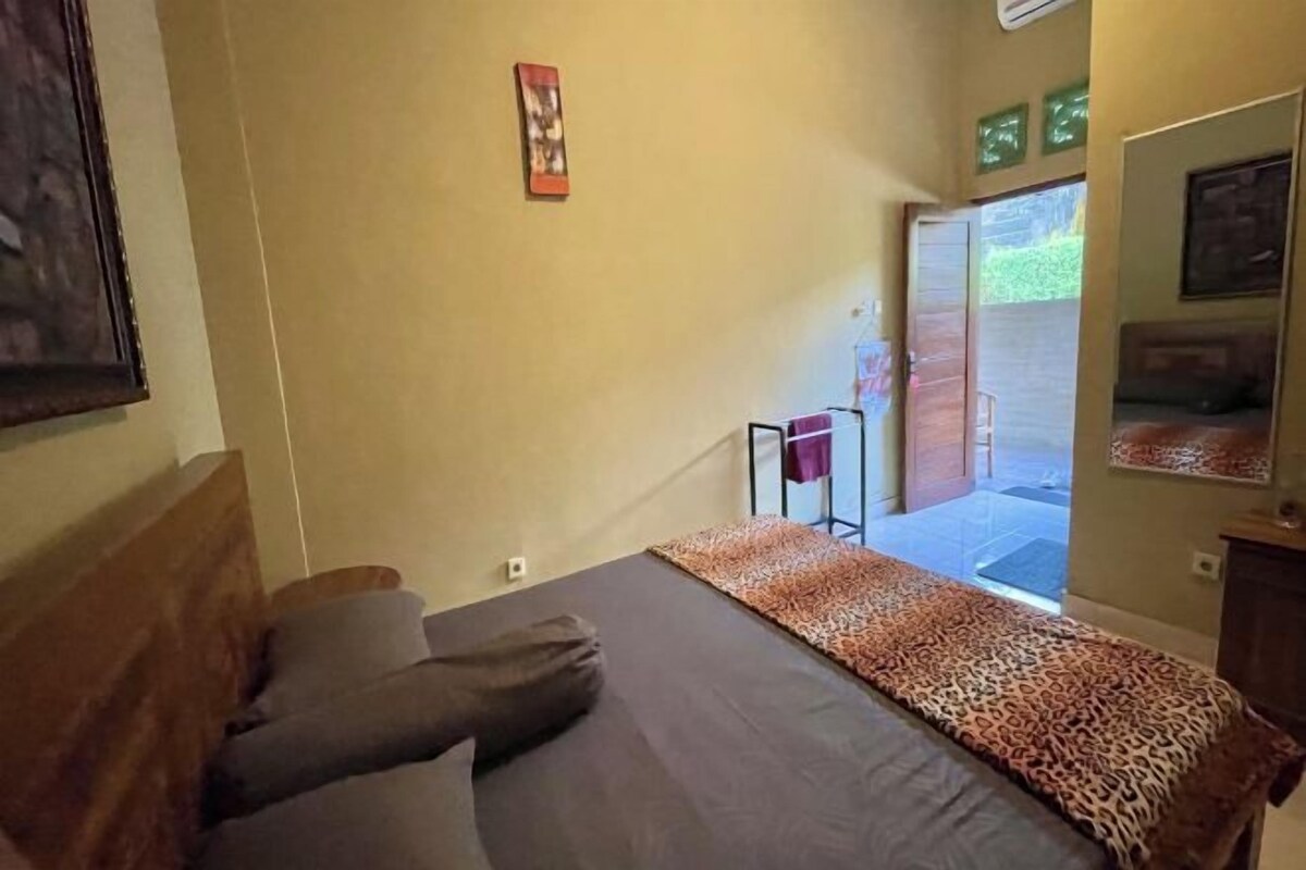 A bedroom with a bed, a wooden headboard, a leopard print bedspread, and a small table with a purple towel.