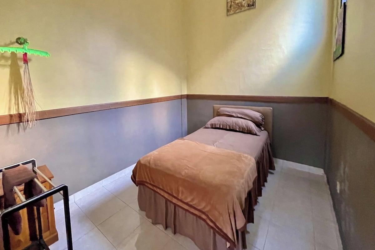 Une petite chambre à coucher, bien rangée, avec un lit simple, une petite table et une chaise.