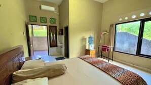 A hotel room with a bed, a water dispenser, a small table, and a view of greenery outside. - Mongan Homestay Beside The Belulang Hot Spring (Penebel)
