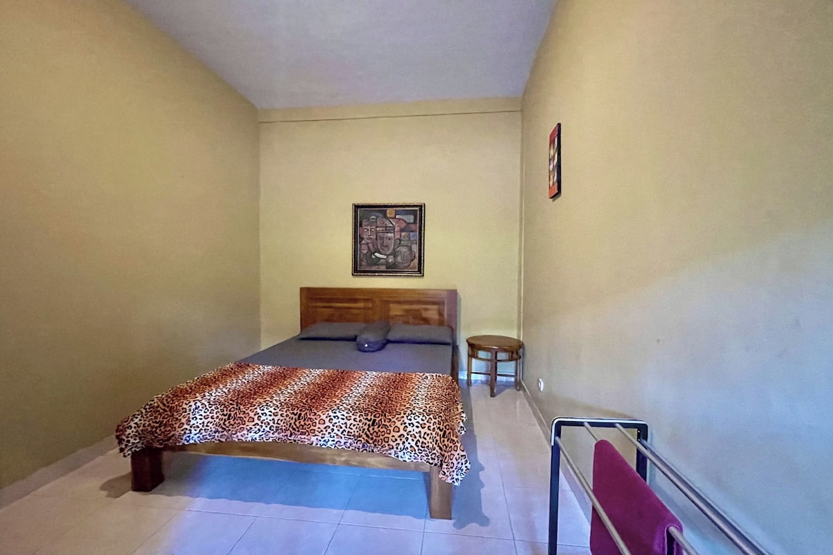 Une chambre à coucher avec un lit, un petit tabouret et un tableau accroché au mur.