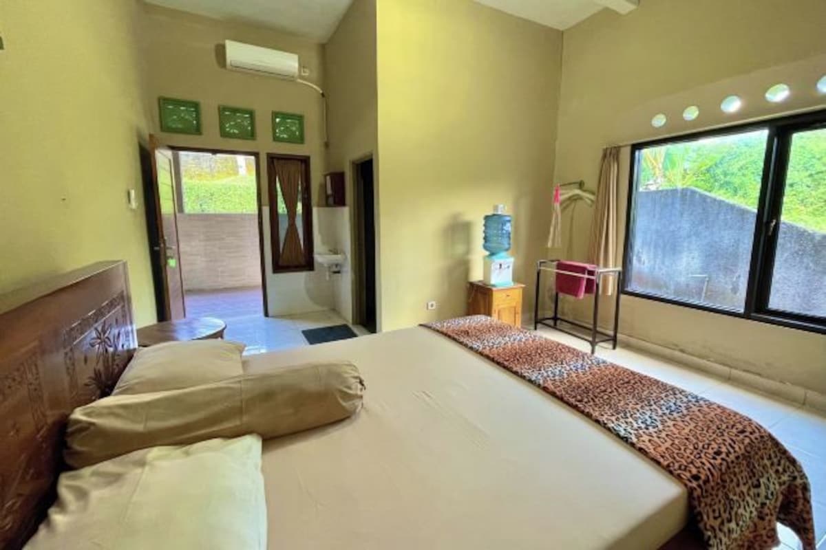 Une chambre d’hôtel avec un lit, un distributeur d’eau, une petite table et une fenêtre donnant sur un espace verdoyant.