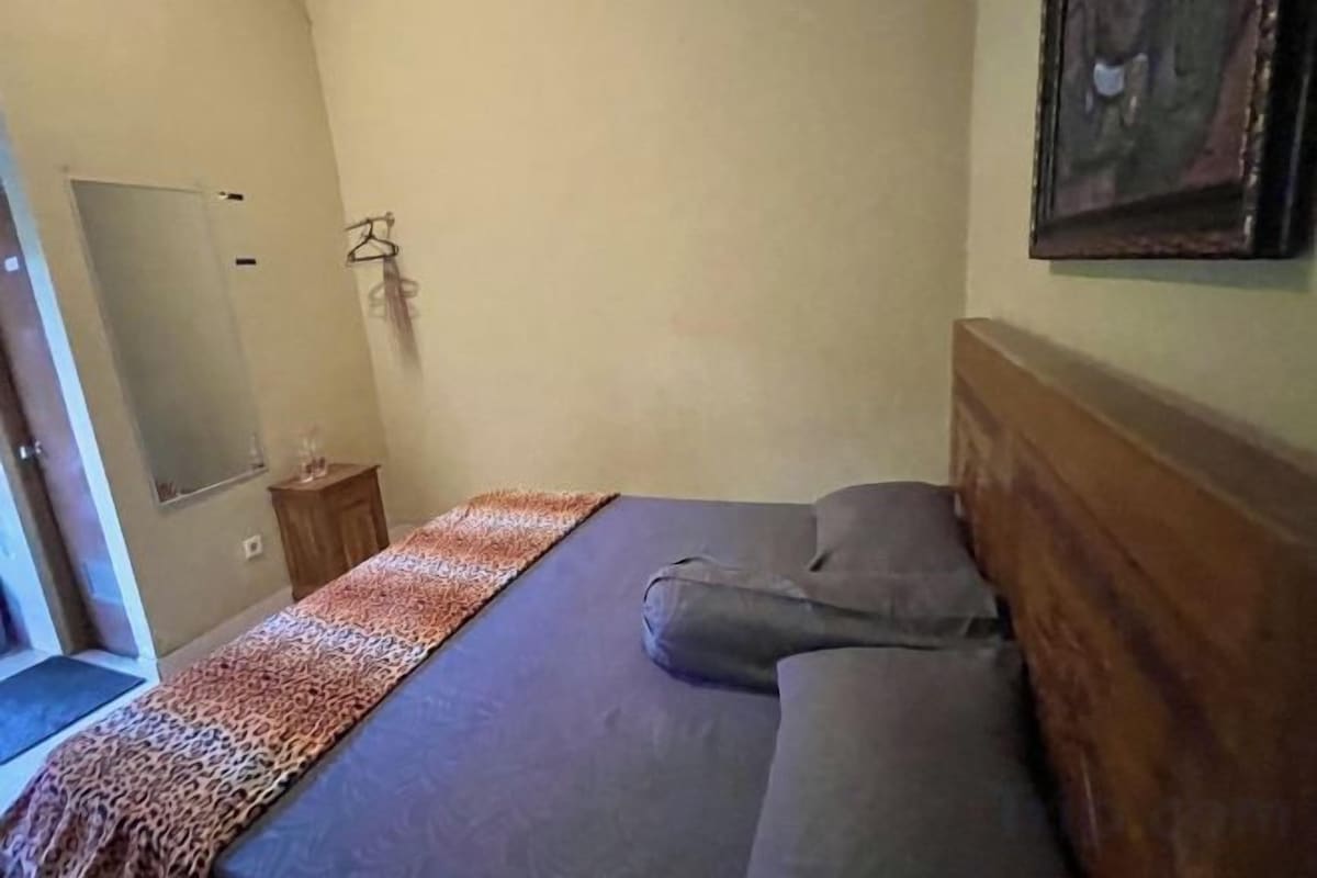 A bedroom with a bed, a wooden headboard, a bedside table, and a mirror.