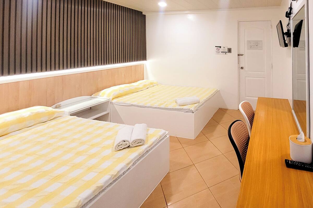 Ein Hotelzimmer mit zwei Betten, einem Holztisch, einem Stuhl und einer Badezimmertür.
