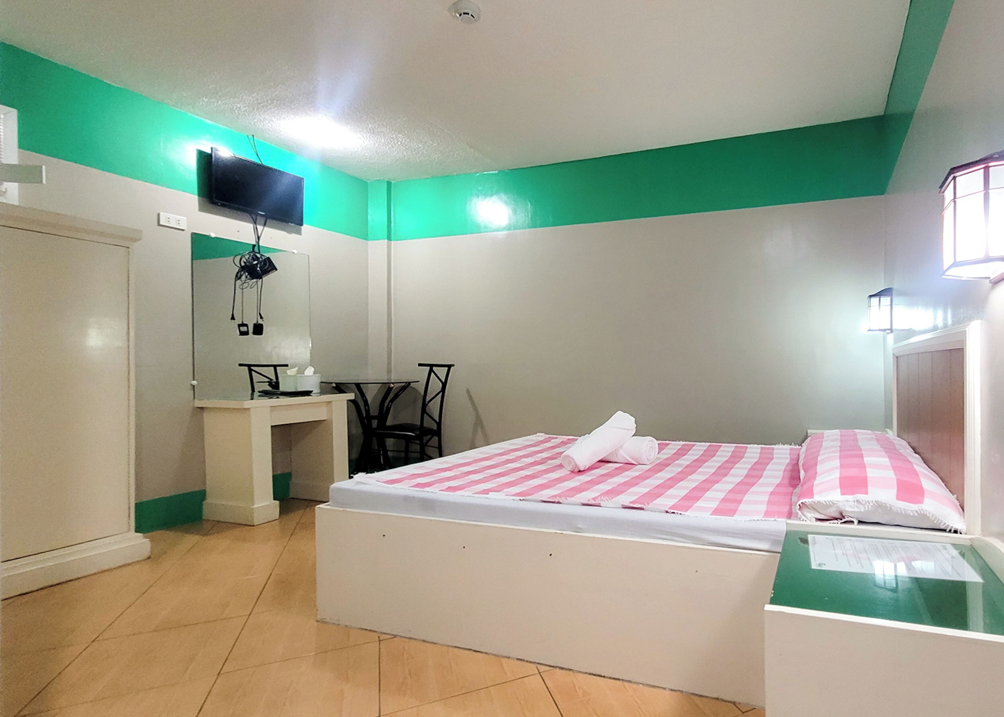 A bedroom with a bed, a desk, a chair, a TV, and a window.