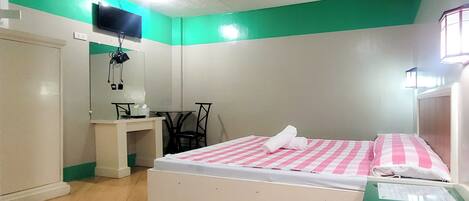 A bedroom with a bed, a desk, a chair, a TV, and a window.