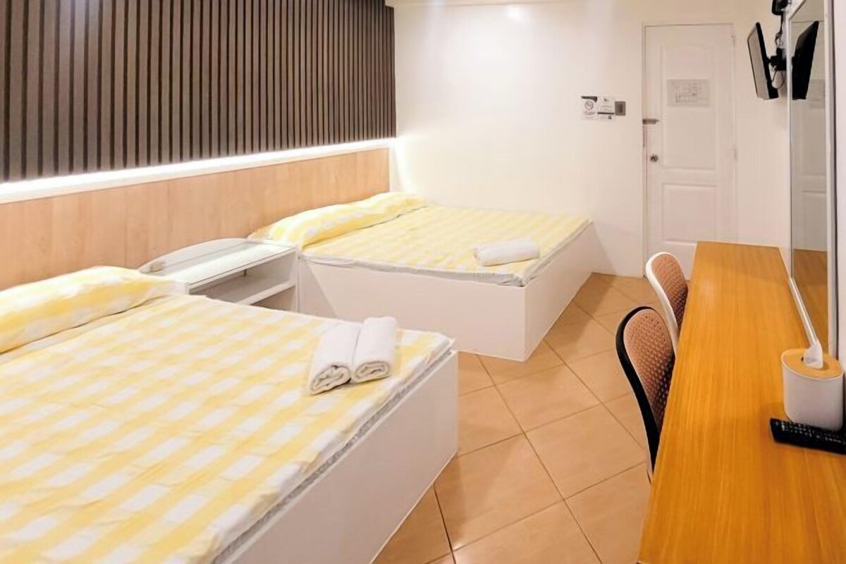 Habitación de hotel con dos camas, un escritorio de madera, una silla y una puerta blanca.