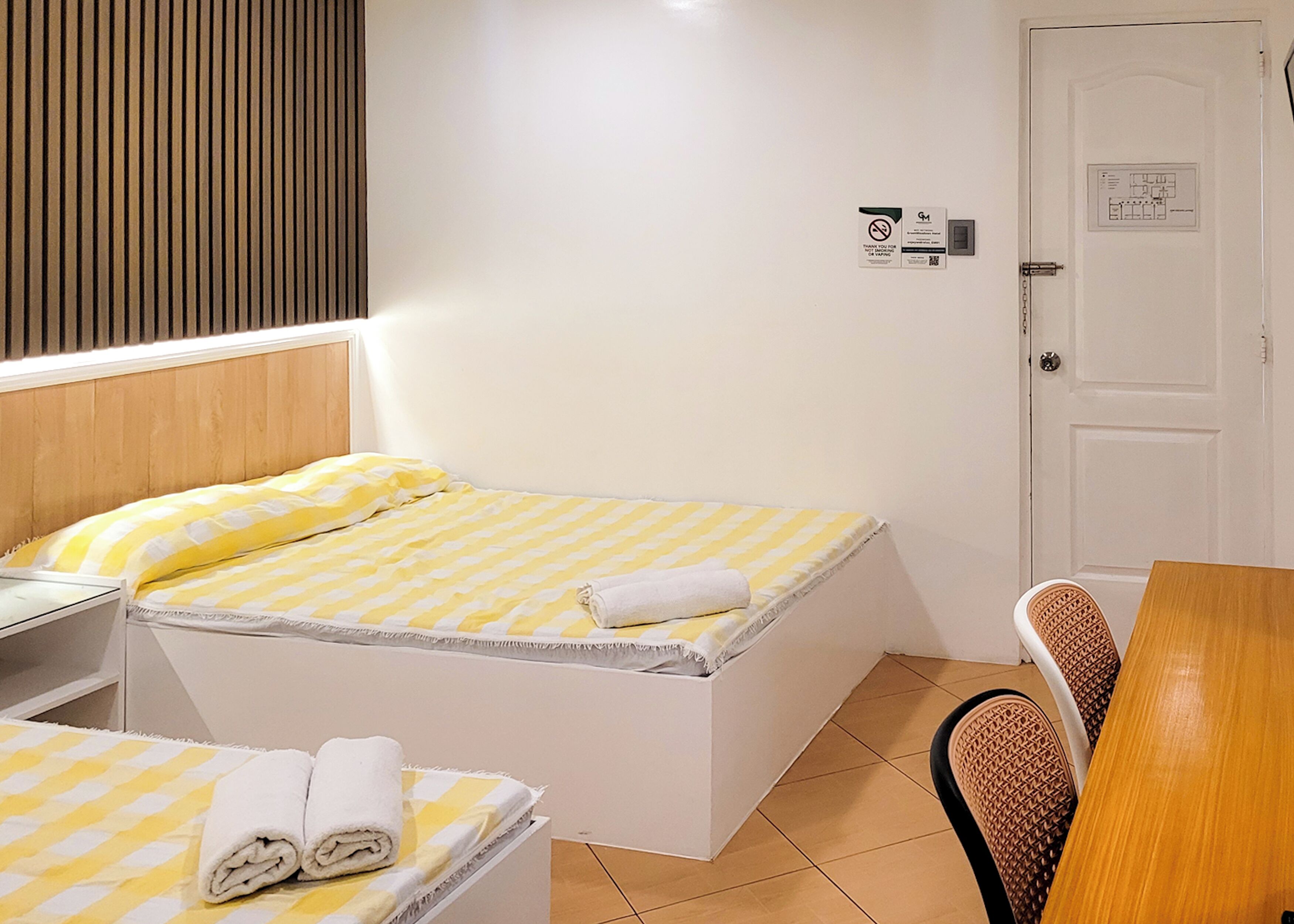 Una camera da letto piccola e ordinata, con un letto, un comodino, una sedia e una porta con un cartello.