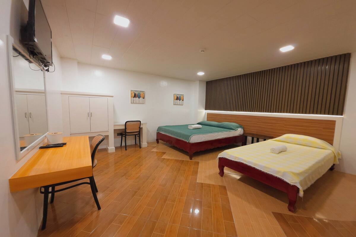 Ein Hotelzimmer mit zwei Betten, einem Schreibtisch, einem Stuhl und einem an der Wand befestigten Fernseher.